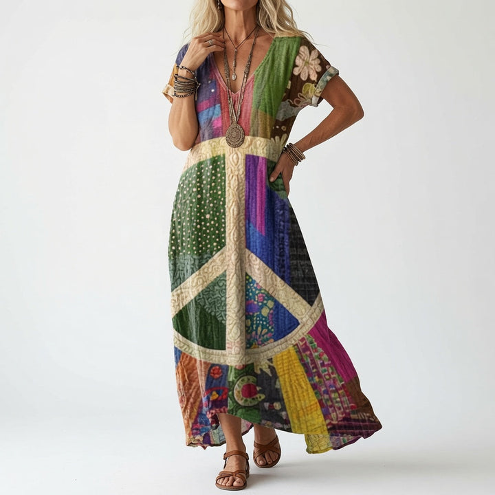 Woman in a colorful patchwork V-neck dress with a large cream peace symbol on the front, worn with brown leather sandals.