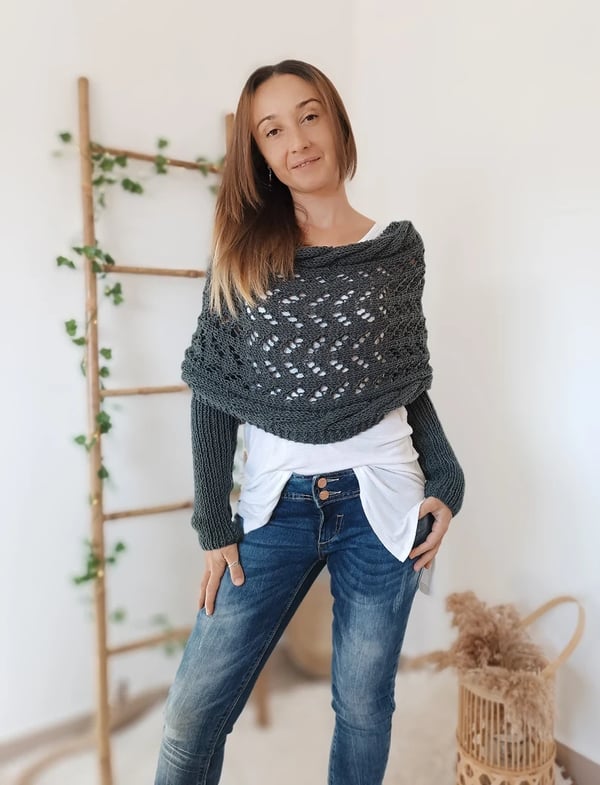 Woman wears the charcoal gray wrap with built-in sleeves, standing with one hand in her pocket beside a wicker basket. 14