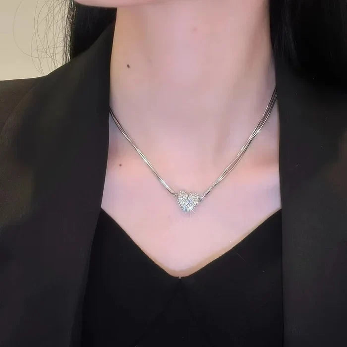 Straight-on view of the rhinestone heart necklace on a model wearing a black blazer and V-neck top, with light catching the stones. 6