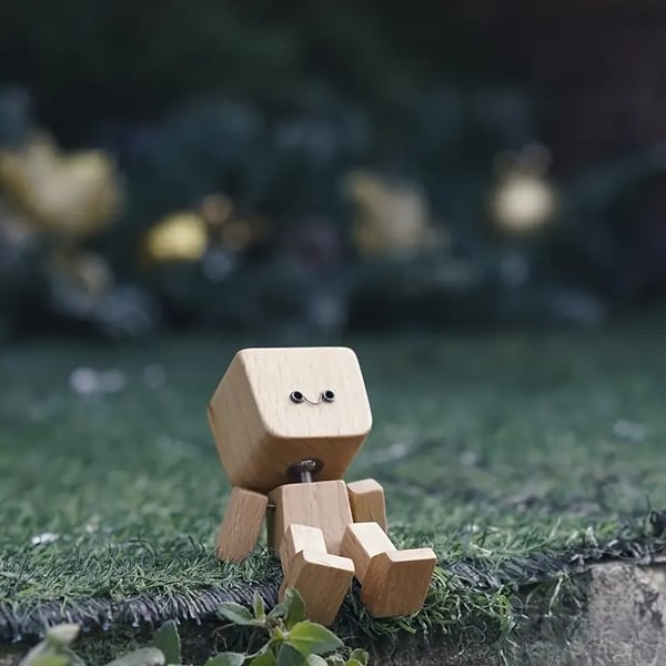 Wooden figure with a smiling face sits on artificial grass outdoors against a blurred green background 5