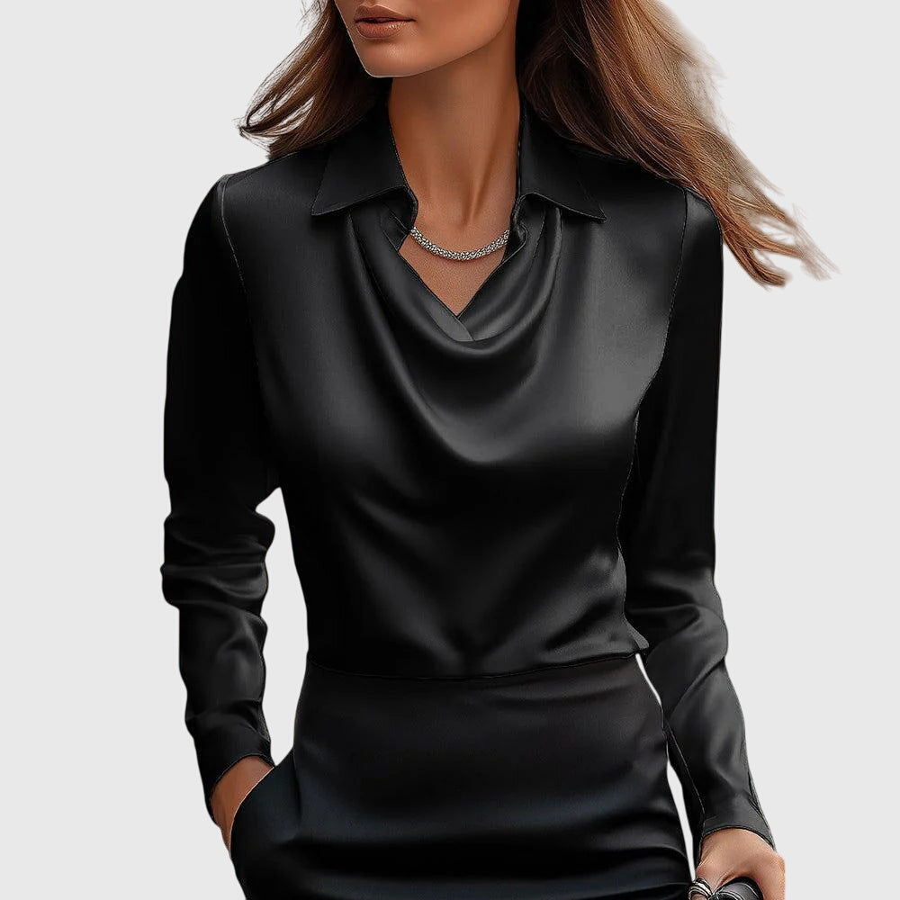 Model wearing the blouse in solid black satin with draped cowl neck and collar, paired with a black skirt and slim silver necklace.
