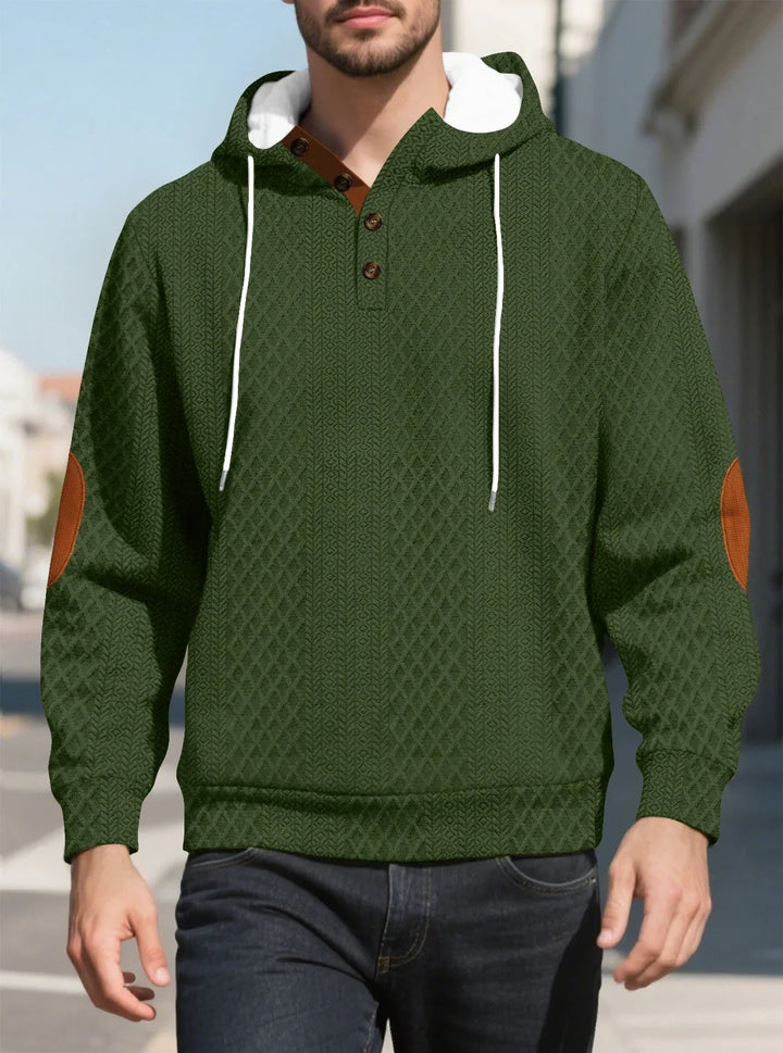 Man walking outdoors in the olive green diamond-textured hoodie, front view with brown elbow patches 22