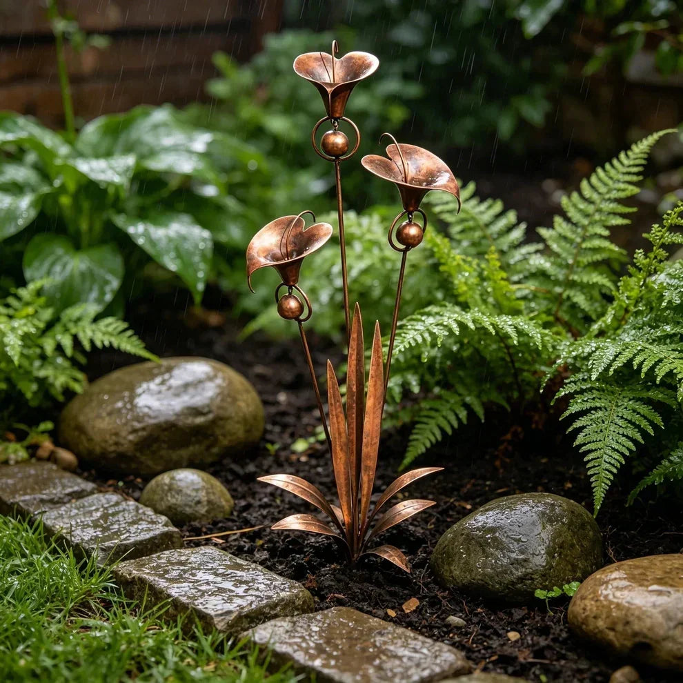 Copper bloom stake in a rainy shaded garden bed, droplets on the metal, surrounded by ferns, hostas and wet stones. 3