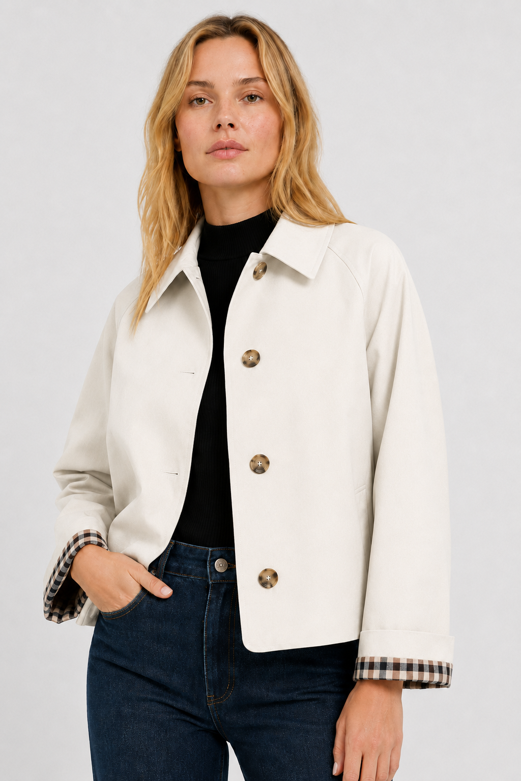 Front view of a model in the cream button-up jacket over a black top and jeans, hand in pocket, checked cuffs showing. 21