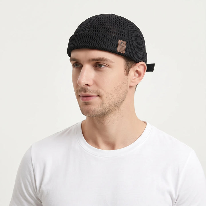 Man in a white tee wears the black open-weave brimless cap with a rolled cuff and leather patch 24