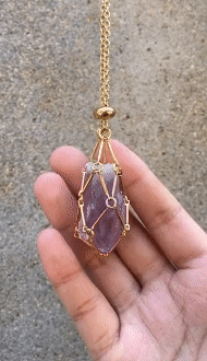 Gold chain necklace with a wire-cage pendant holding a rough purple crystal on an open palm. 5