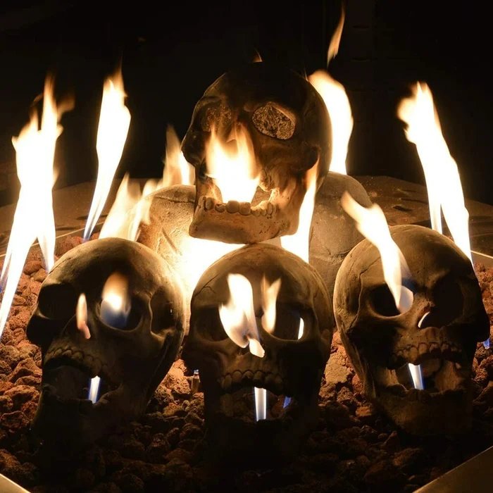 Another view of four skulls on lava rock in a fire feature at night with tall flames.