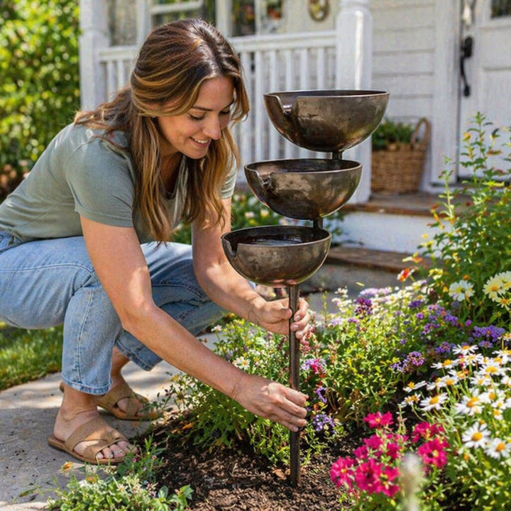 Brown stainless-steel bird bath stake being pushed into a garden bed.