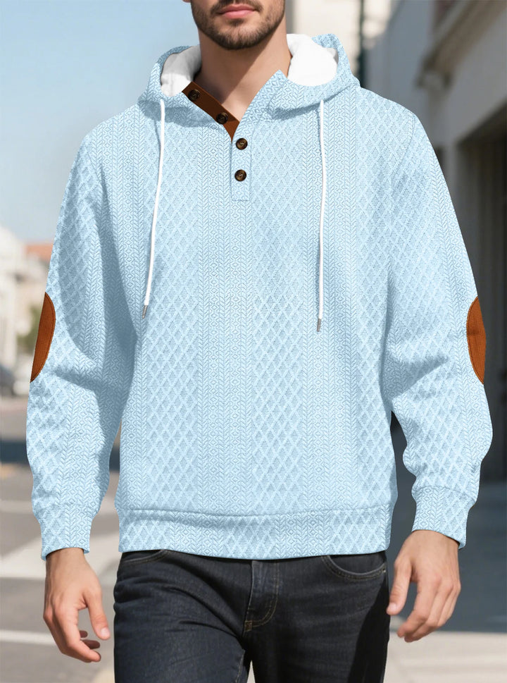 Man walking outdoors in the light blue diamond-textured hoodie, front view with brown elbow patches 29