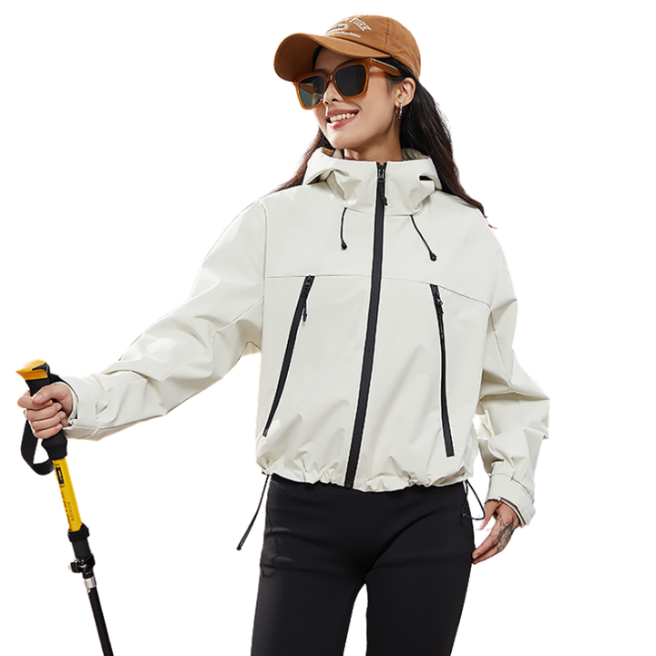 Smiling model in the cream hooded jacket with a brown cap and sunglasses, holding a trekking pole, hem drawcord cinched. 3