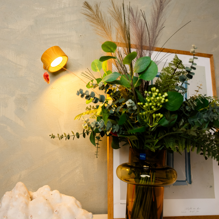 Black wireless LED wall light, another view, beside a framed print and vase arrangement.
