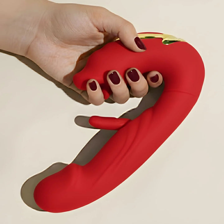 Hand with dark red nails gripping the handle of a red silicone dual-motor massager, showing its curved shape and small gold accent. 5