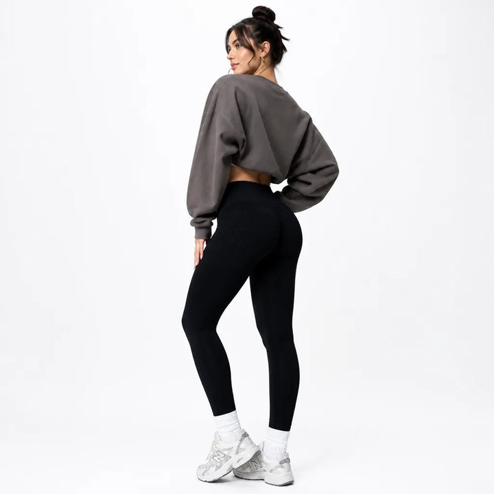 Model glancing over her shoulder in black high-waisted leggings, a gray cropped sweatshirt, and white sneakers, seen from behind. 4