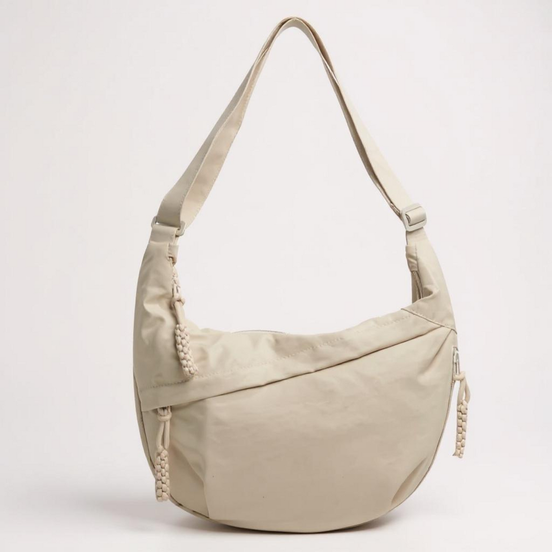Beige crescent-shaped nylon bag with a single adjustable strap and braided zipper pulls.