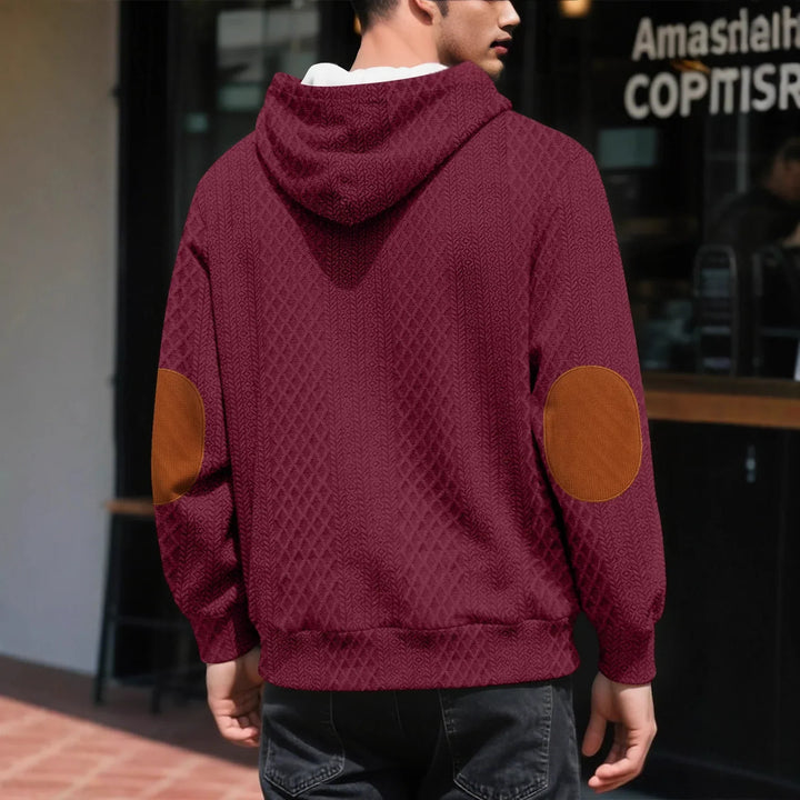 Back view of a burgundy diamond-knit hoodie with brown elbow patches, worn outside a storefront 2