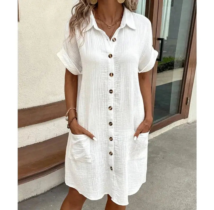White textured button-front dress with cuffed sleeves, cropped on a model with hands in pockets outdoors 2