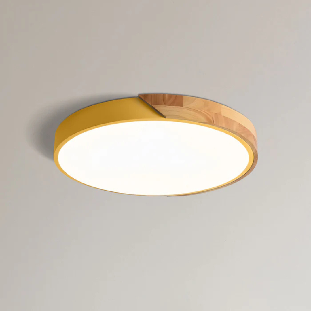 Yellow round ceiling light with a natural wood section on the rim, mounted on a light ceiling and glowing white.