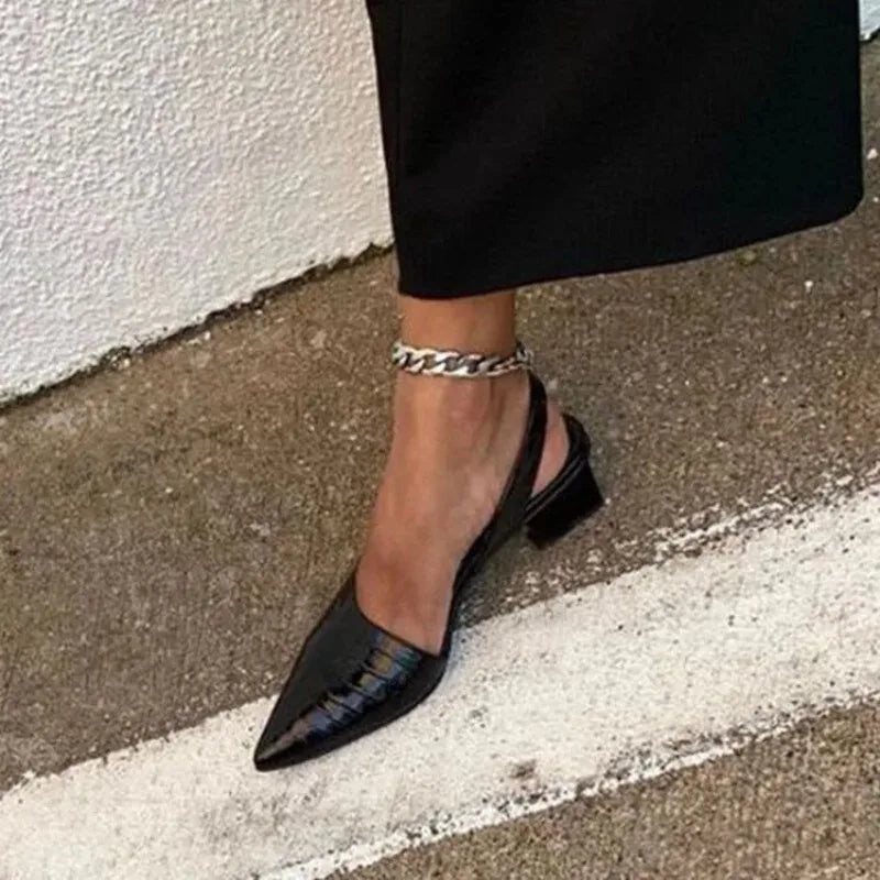 Close-up of a foot in a black croc-embossed pointed slingback with a silver chain anklet 2