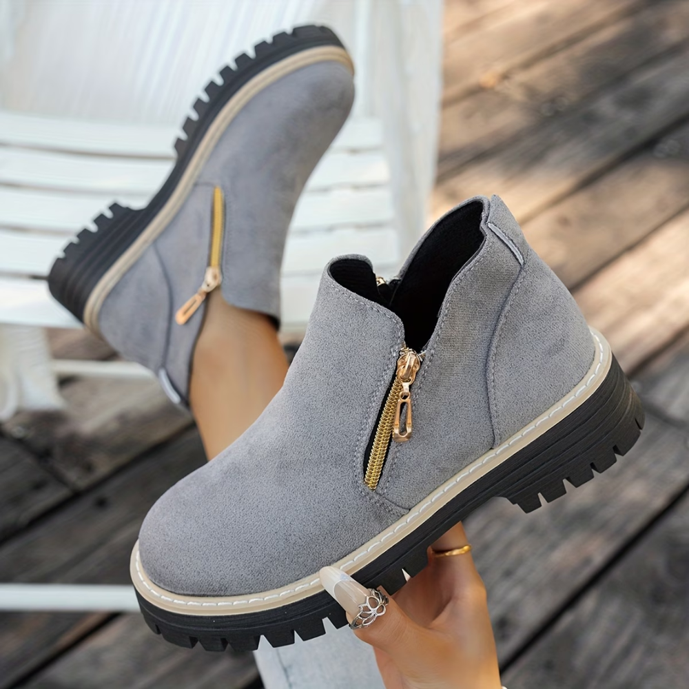 Gray suede-look ankle boots with gold side zippers and chunky black lug soles.