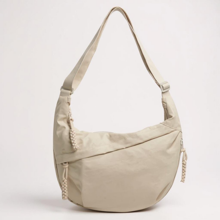 Beige crescent shoulder bag with a tonal adjustable strap and braided zipper pulls, another view.