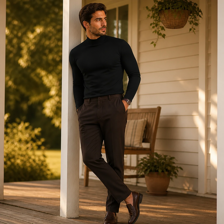 Man wearing the black high-neck tee and brown trousers leaning on a white porch post.