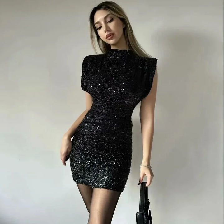 Model wearing black sequined mini dress with sheer tights, holding a small black bag 2