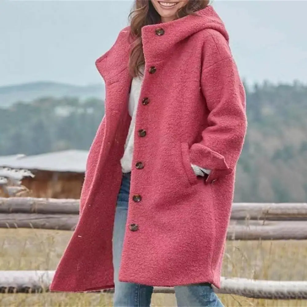 Woman in a coral pink buttoned hooded coat standing by a wooden fence outdoors 2
