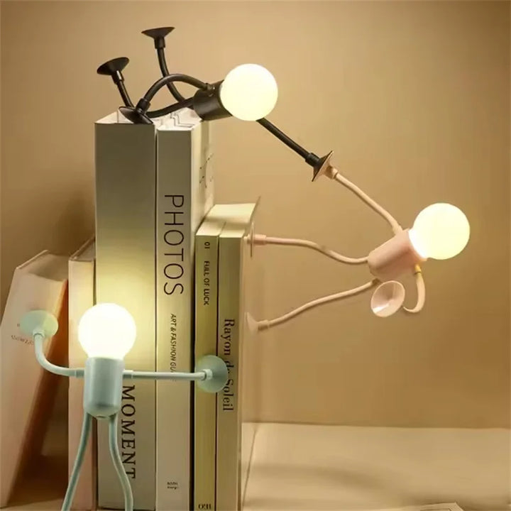 Three posable figure lights in black, pink and green climbing a stack of books, bulbs glowing 2