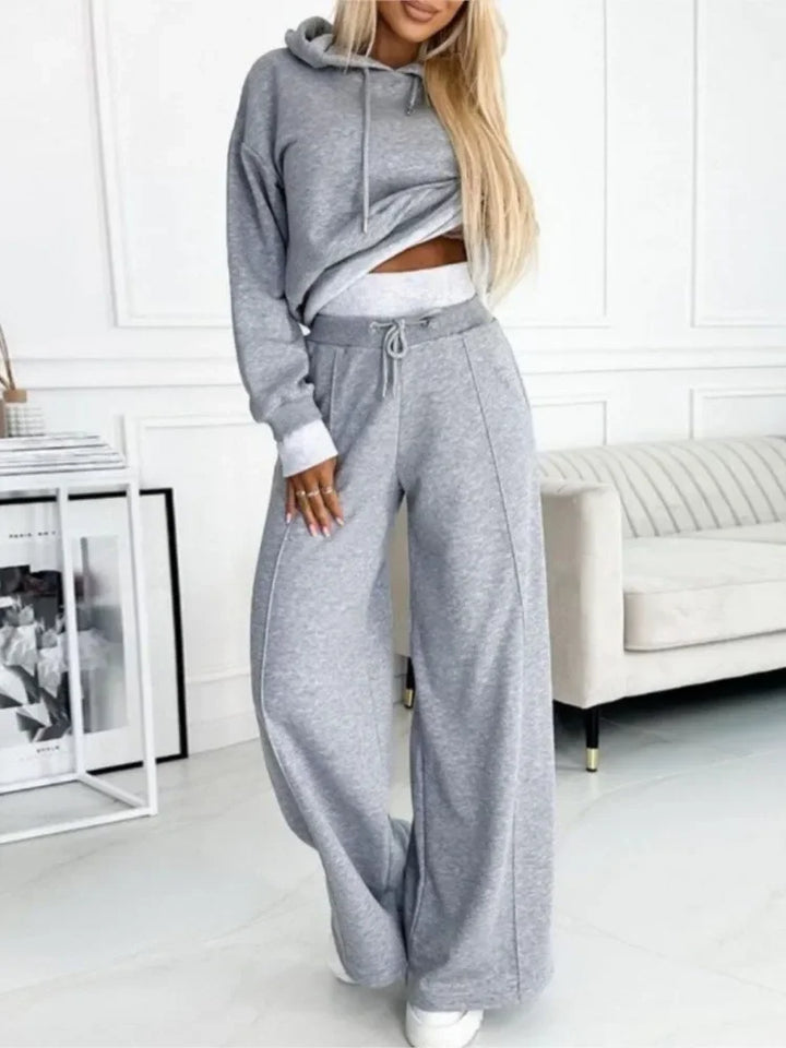 Model in a gray hoodie and wide-leg drawstring pants with light contrast trim, in a bright living room 2
