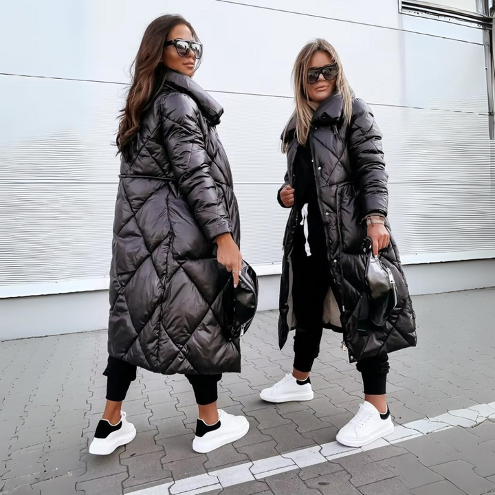 Two women pose in black quilted long coats, one seen from the back.