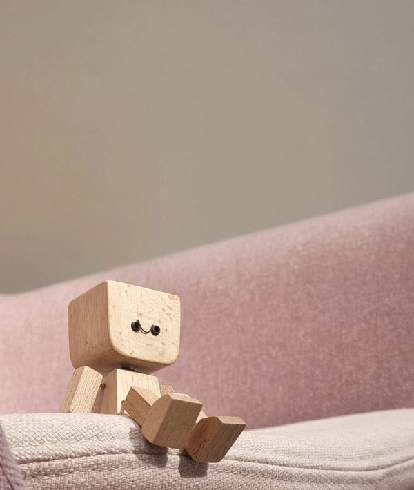 Small wooden figure with a smiley face sits on the arm of a pink fabric sofa 4