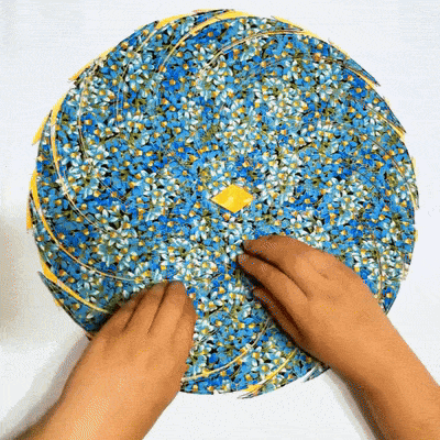 Hands arranging curved blue floral fabric pieces into a round spiral placemat template.