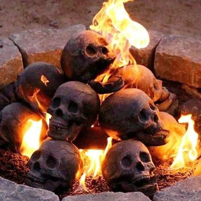 Ceramic skulls stacked inside a stone-ringed fire pit with bright orange flames.