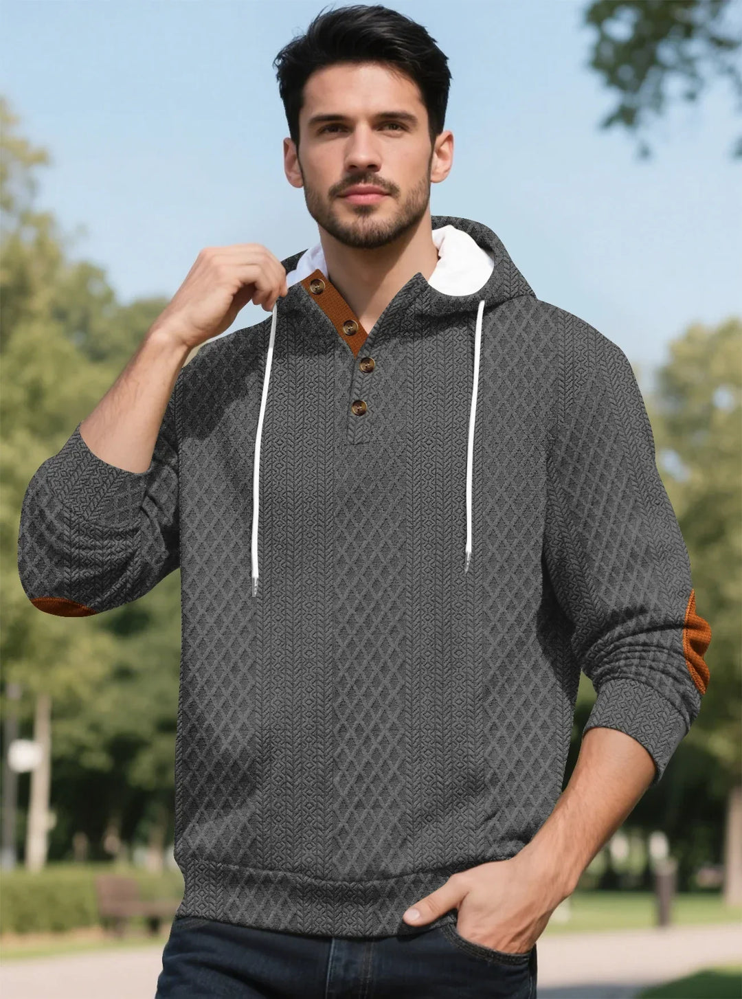 Man in the gray textured hoodie holding a drawstring, standing in a park 33