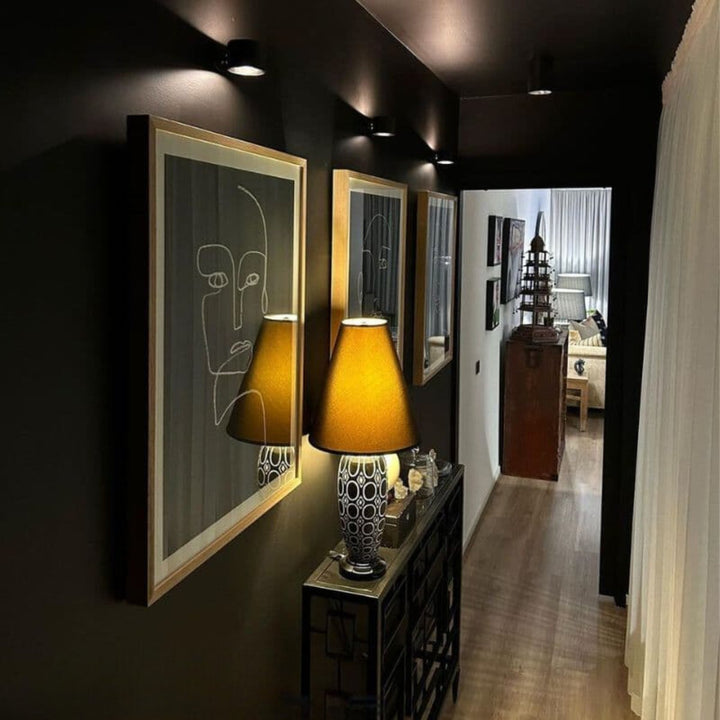 Black wireless LED wall lights, another view, along a hallway above framed portraits.
