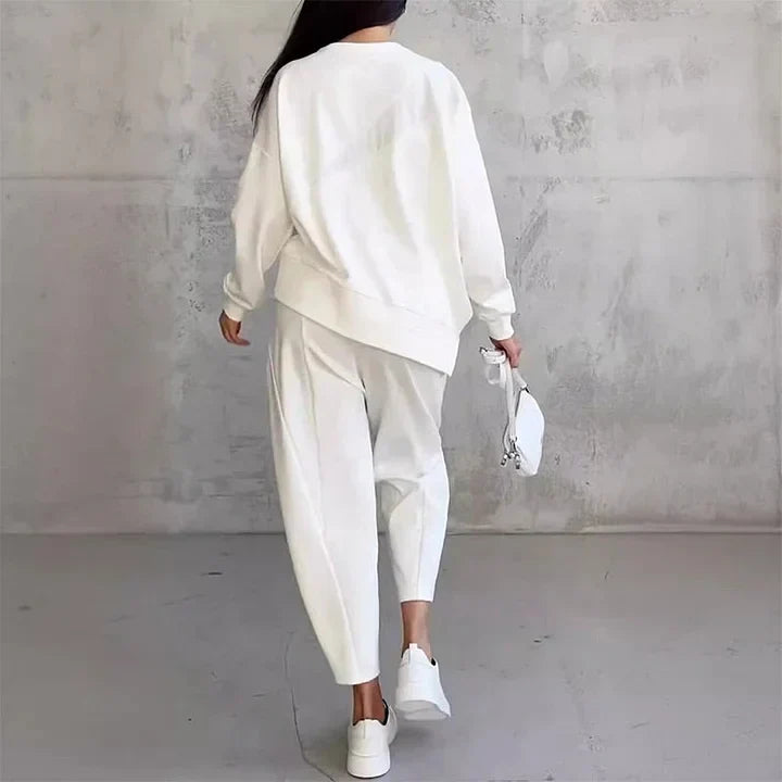 Back view of the white set on a woman walking away, showing the sweatshirt's curved hem and the joggers' seam details.