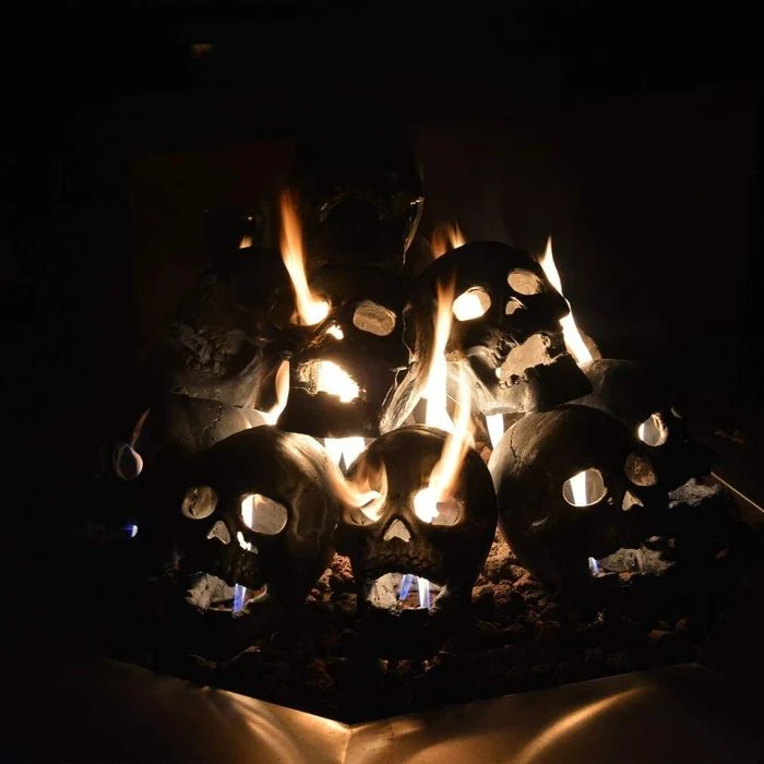 Another view of a pyramid of skulls in a dark fire pit with flames through their eye sockets and open mouths.