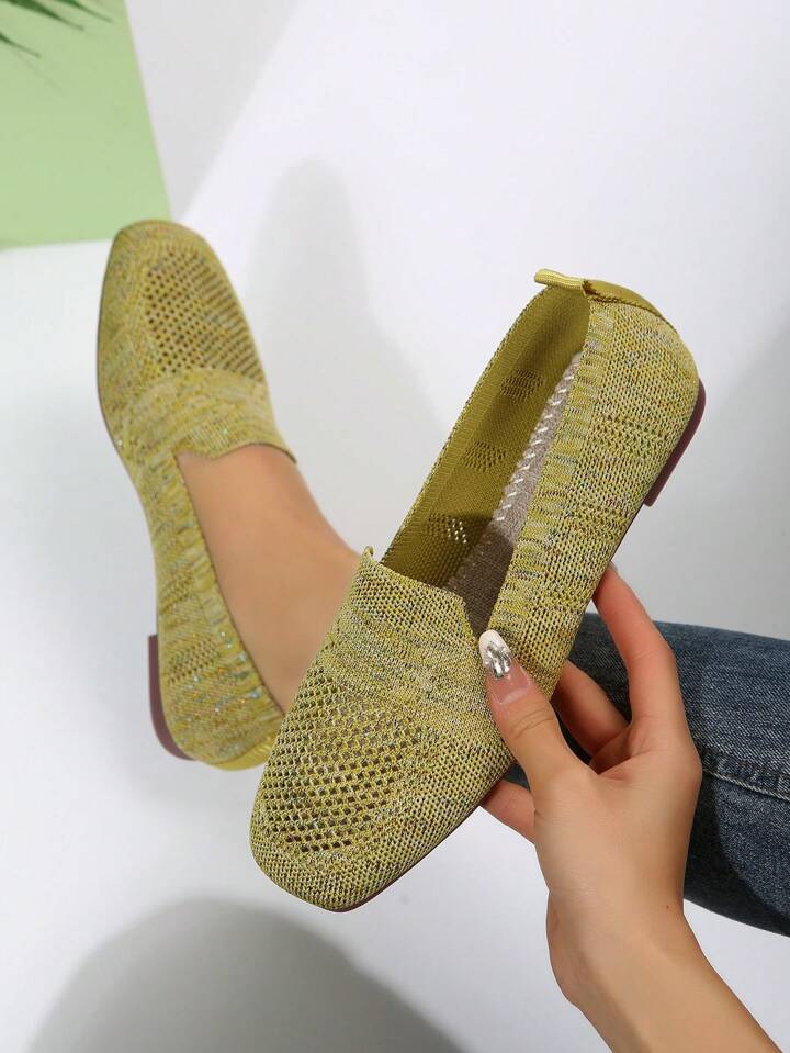 Olive-yellow knit flats showing the inside and woven insole, one held in a hand.
