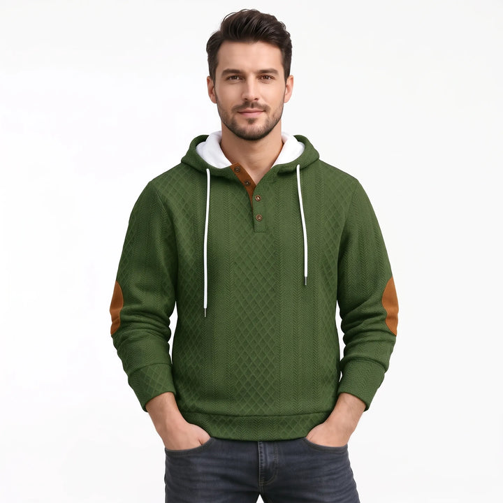 Studio shot of a man in the olive green textured hoodie with hands in pockets 39
