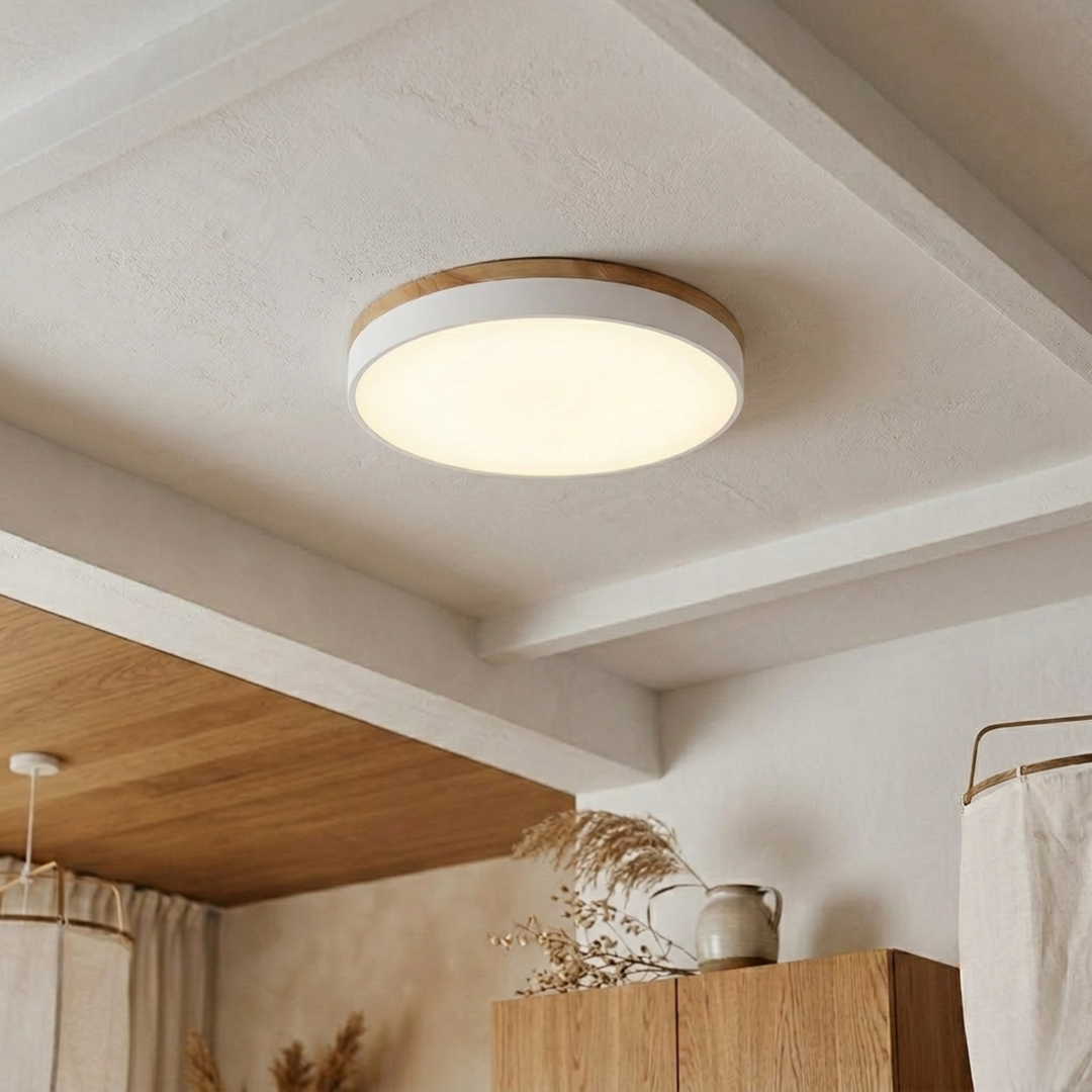 White flush-mount disc light with wood-grain top trim glowing warm on a beamed plaster ceiling above wooden cabinets. 10