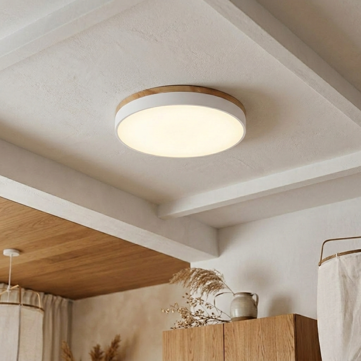 White flush-mount disc light with wood-grain top trim glowing warm on a beamed plaster ceiling above wooden cabinets. 10