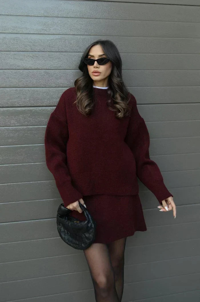 Model in a burgundy knit sweater and matching mini skirt, holding a black woven clutch 1
