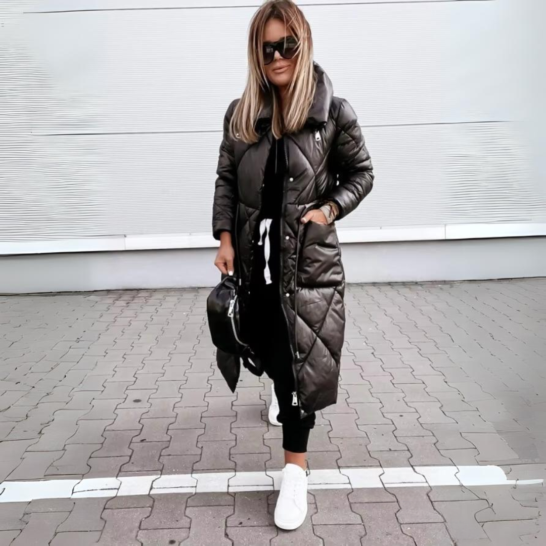 Black quilted long coat worn with one hand in a pocket, white sneakers, and a black bag.