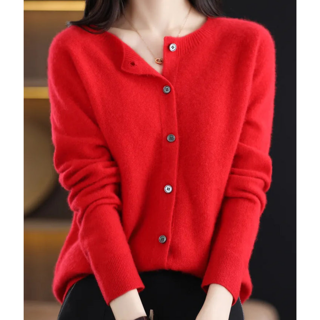 Woman wearing a bright red round-neck button cardigan with a pendant necklace, seated and styled with black pants. 14