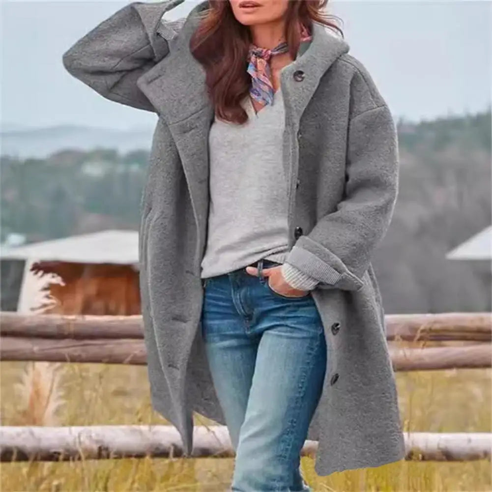 Gray fleece-like hooded coat worn open with a scarf, one hand raised, by a fence 3