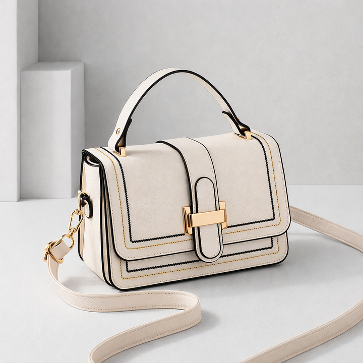 Cream flap bag with gold clasp, top handle and long strap, angled three-quarter view on a pale studio backdrop. 1