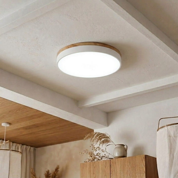 White disc ceiling light with wood-grain trim shining bright cool white on a beamed plaster ceiling. 17