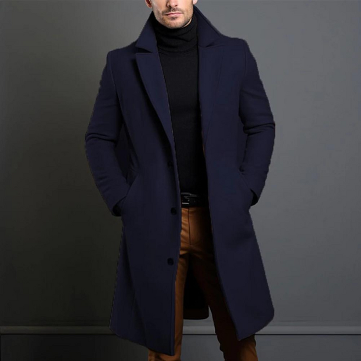 Navy blue longline coat with notch lapels and dark buttons, worn with a black turtleneck and brown trousers, cropped at the chin. 4
