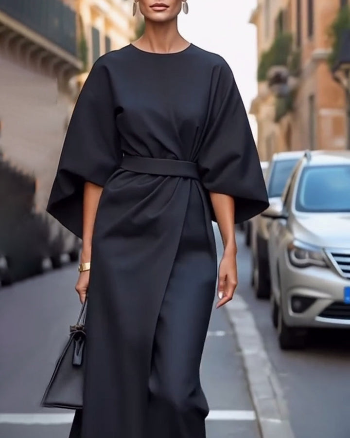 Black belted dress with a wrap skirt and wide sleeves, worn with earrings and a small black handbag 6