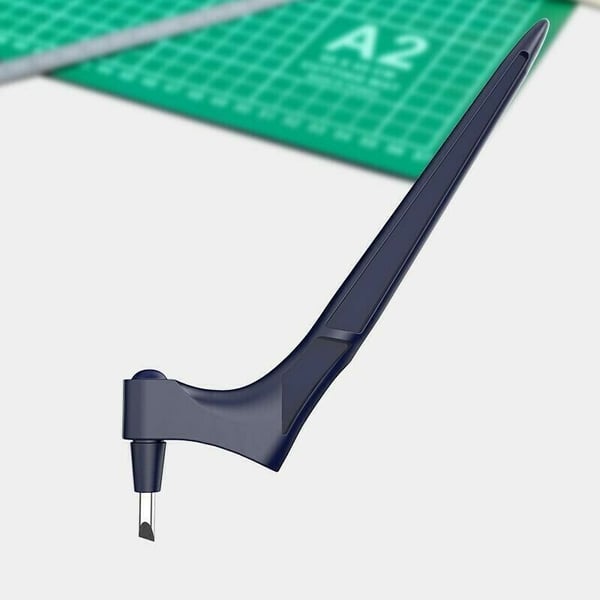 Full side view of the navy swivel-blade craft knife with its angled blade, above a blurred green cutting mat. 14